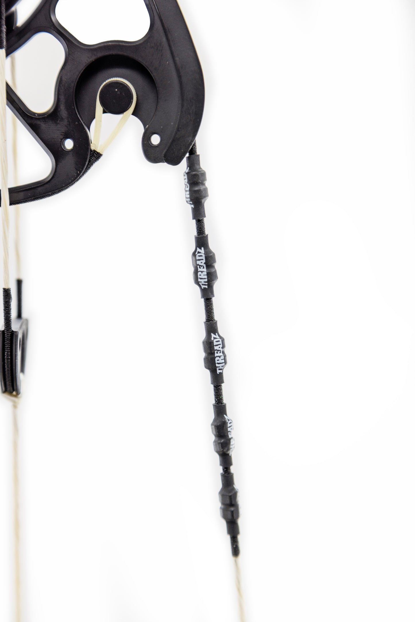 Close-up of a black archery bow cam with white bowstring and black rubber thread protectors labeled "THREADZ."